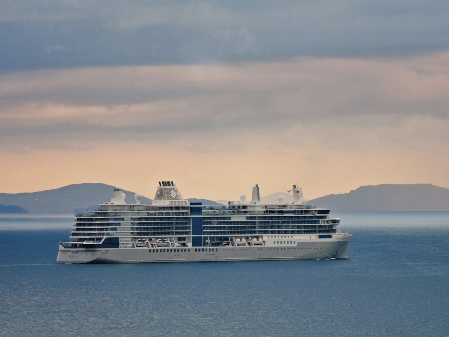 A large cruise ship sails across the calm open ocean.