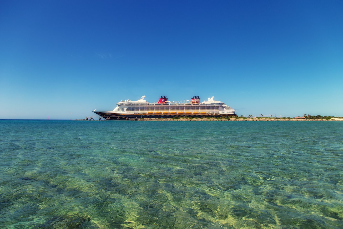 Cruise ship docked at a tropical island with turquoise waters.