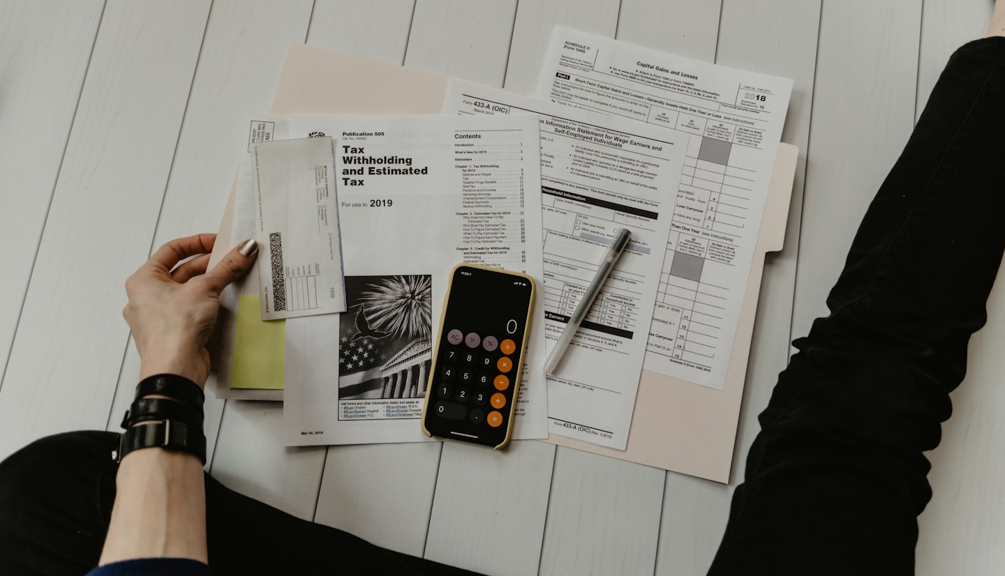 Hands organizing tax forms with smartphone and pen.